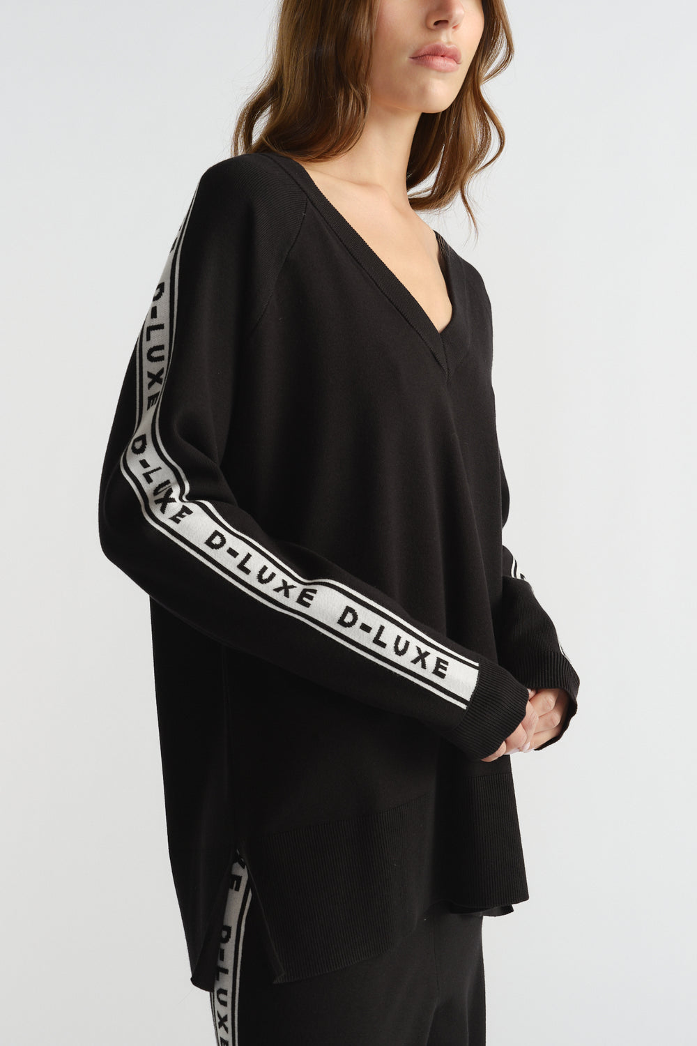Woman wearing a relaxed black knit top with V-neck and white logo stripe detail along the sleeves and side seams