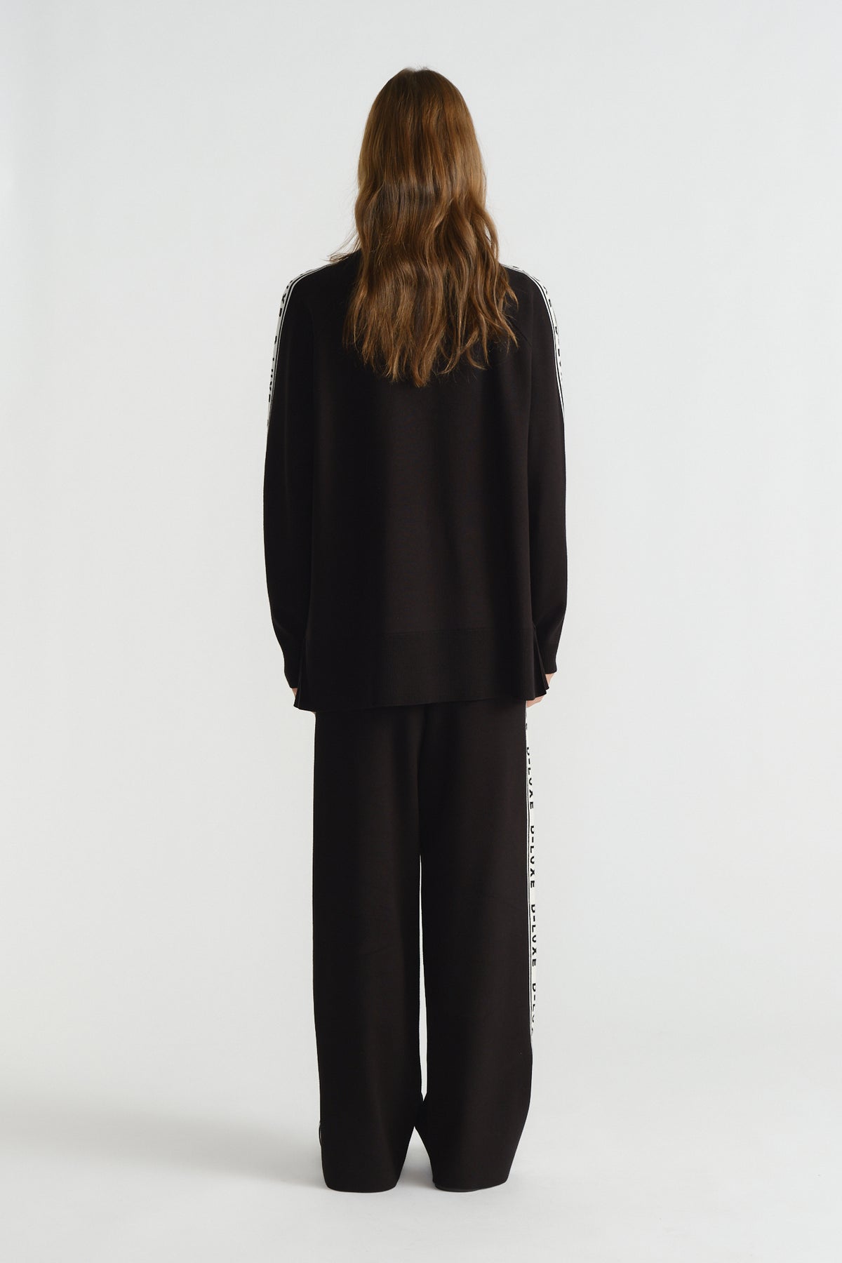 Back view of woman wearing a relaxed fit black knit top and matching wide-leg pants with side logo piping