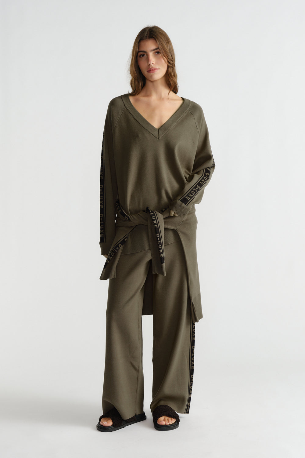 Woman wearing relaxed olive green knit top with matching wide-leg pants featuring side logo panels and tie detail.
