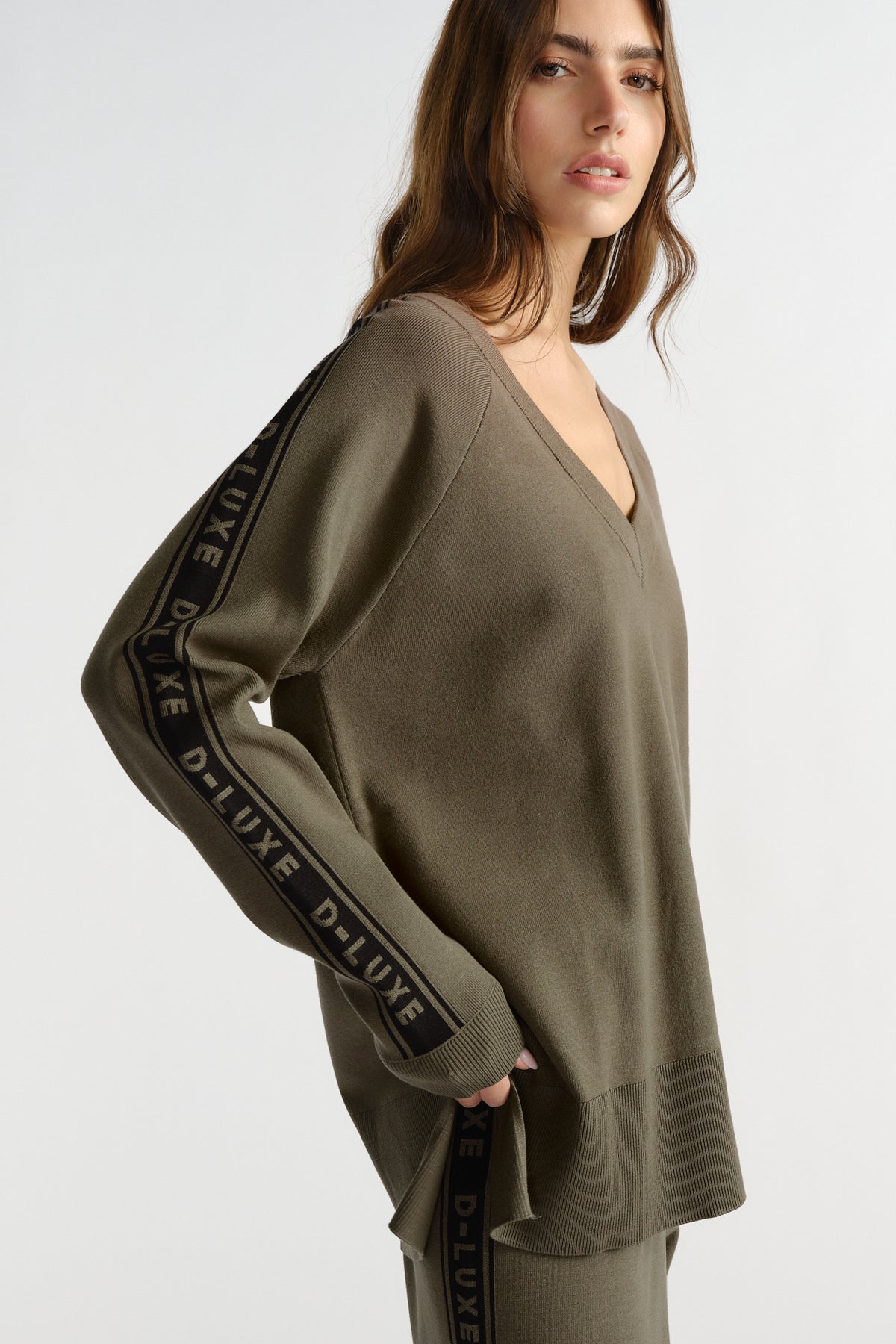 Woman wearing an olive knit top with V-neck and branded tape detail along the sleeves for a relaxed look