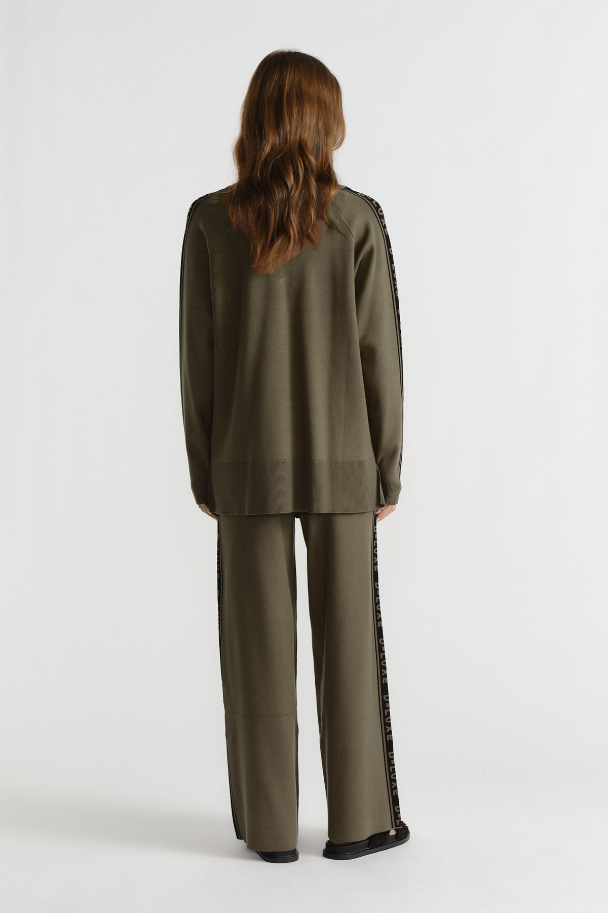Back view of woman wearing olive green knit top and matching wide-leg pants with logo side stripes
