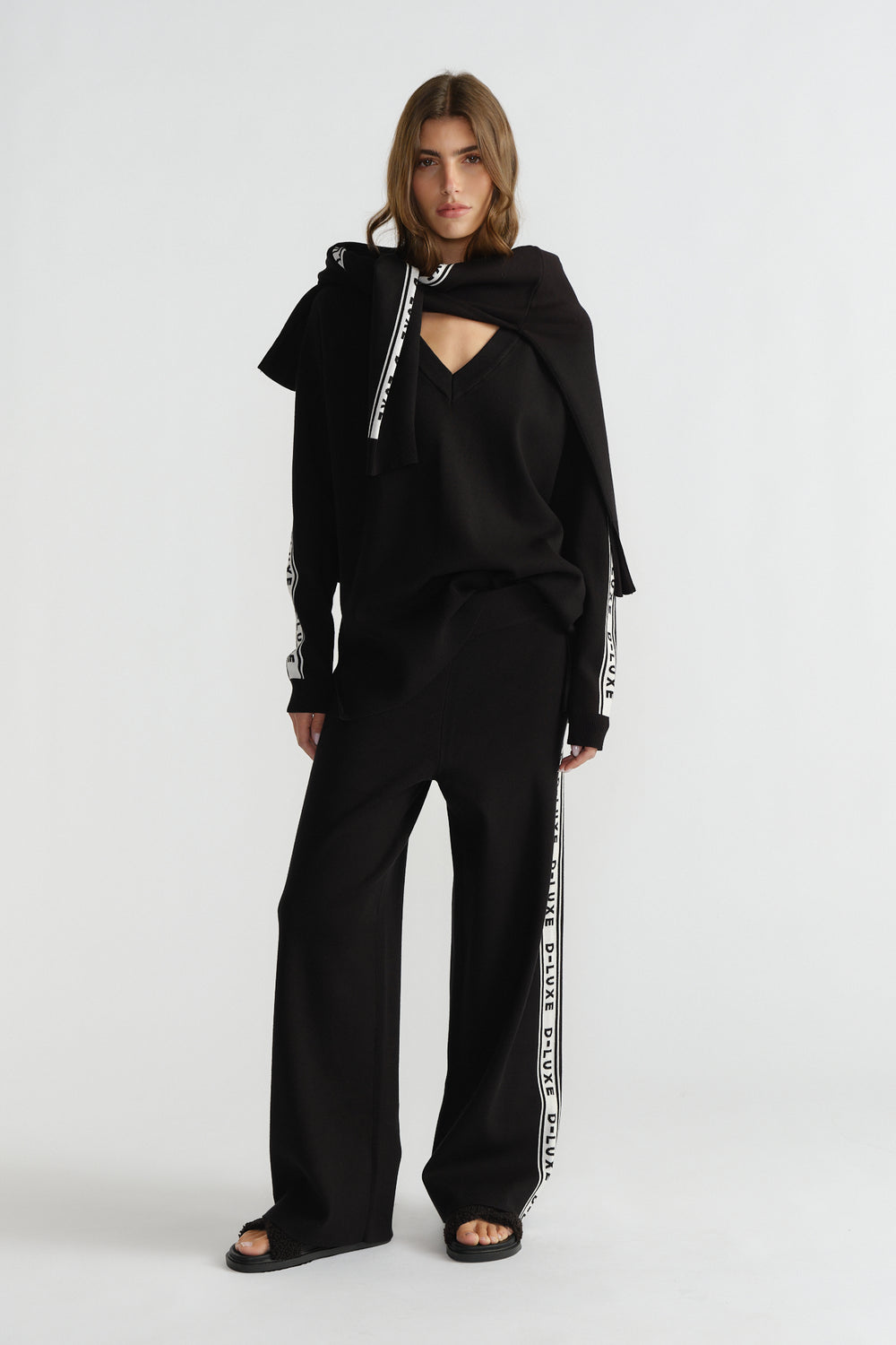 Woman wearing relaxed fit black knit pants with branded side stripes, styled with a matching top and sandals