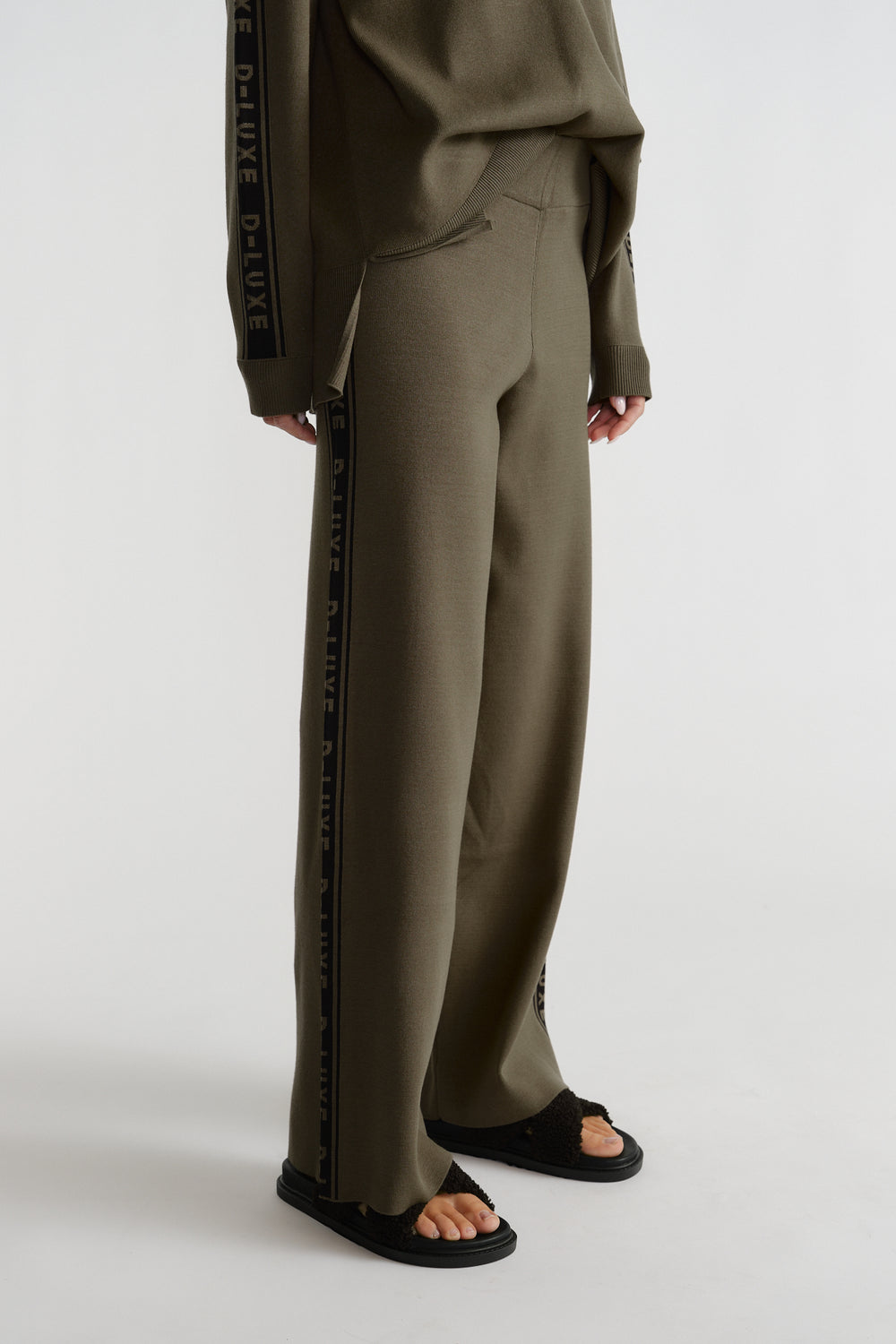 Olive green relaxed-fit knit pants with logo panel stripe down the side, styled with matching top and black sandals