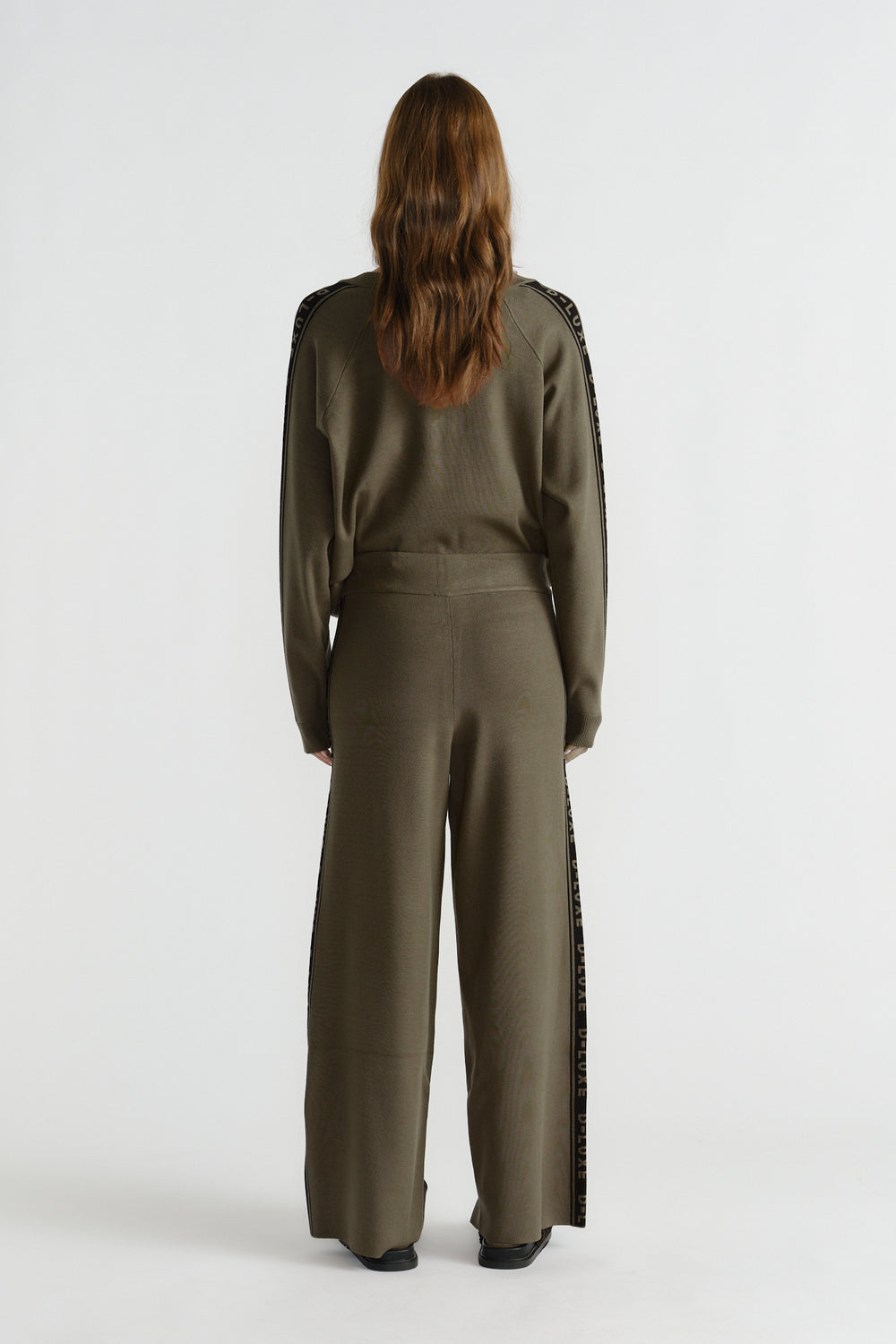 Back view of woman wearing olive green knit pants with logo panel detail down sides and relaxed fit waistband