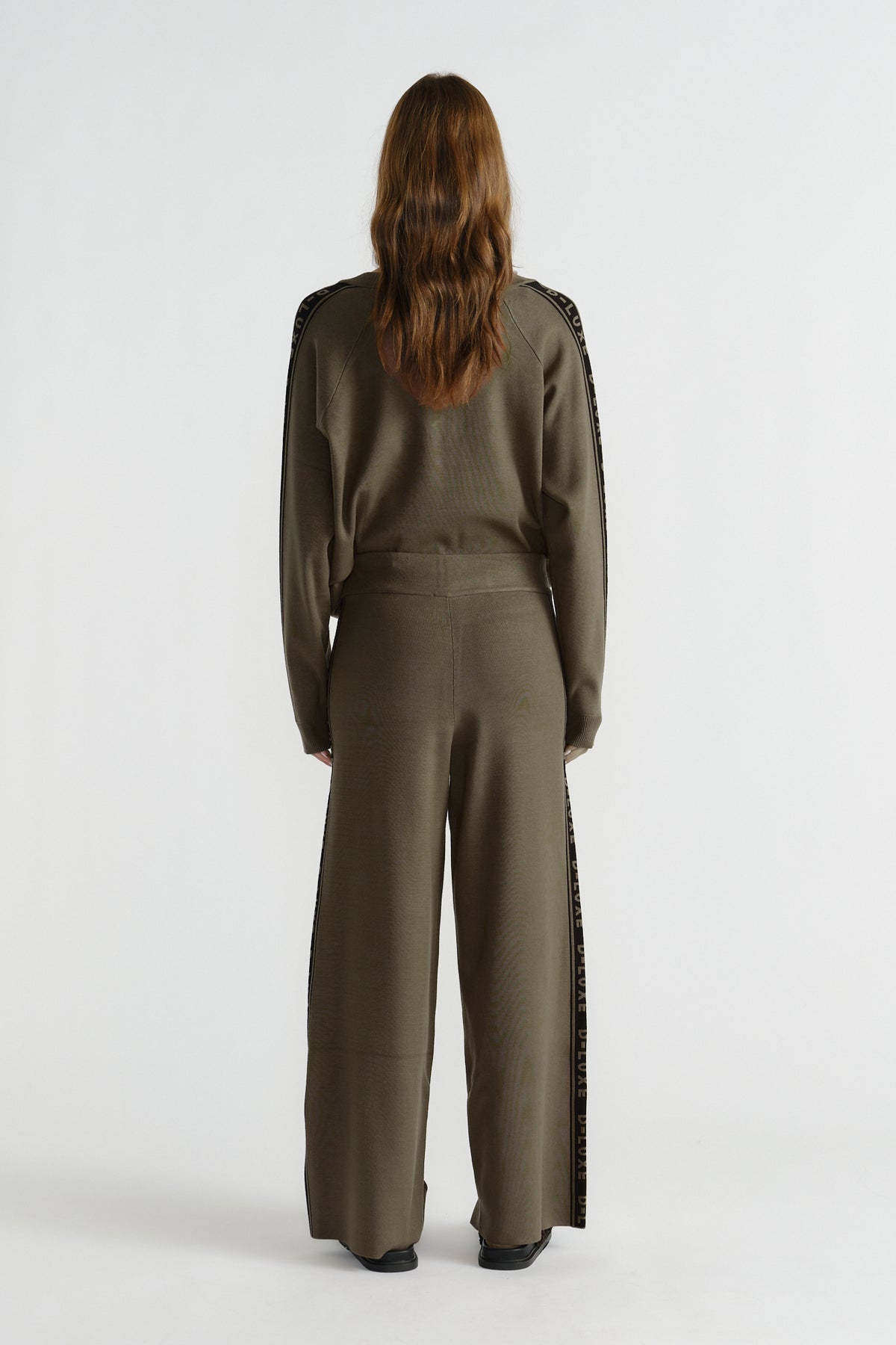 Back view of woman wearing olive green knit pants with logo panel detail down sides and relaxed fit waistband