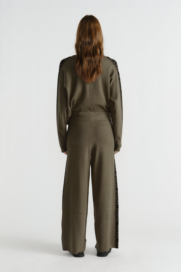 Back view of woman wearing olive green knit pants with logo panel detail down sides and relaxed fit waistband