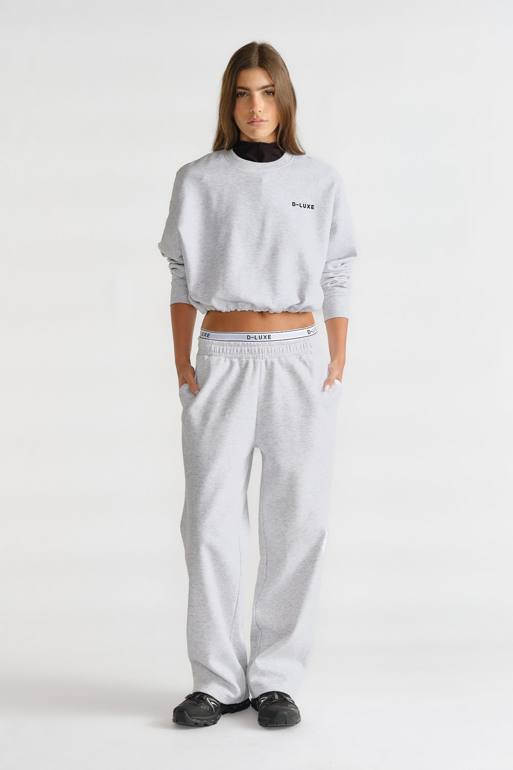 Woman wearing a light grey relaxed-fit trackpant and matching cropped sweatshirt with logo detailing for a casual look