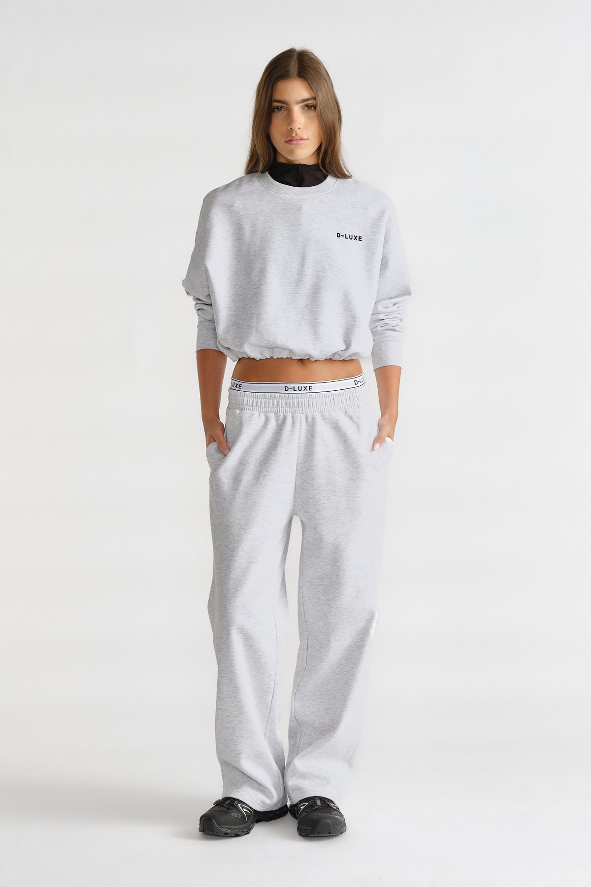 Woman wearing a light grey relaxed-fit trackpant and matching cropped sweatshirt with logo detailing for a casual look