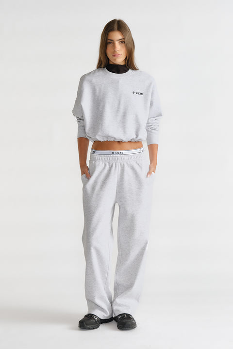 Woman wearing a light grey relaxed-fit trackpant and matching cropped sweatshirt with logo detailing for a casual look