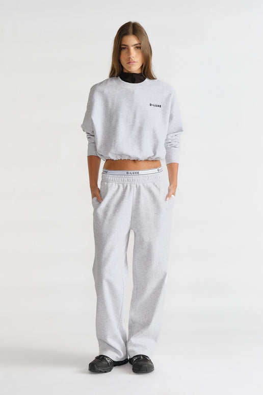 Woman wearing a light grey relaxed-fit trackpant and matching cropped sweatshirt with logo detailing for a casual look