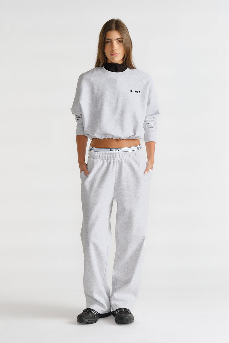 Woman wearing a light grey relaxed-fit trackpant and matching cropped sweatshirt with logo detailing for a casual look