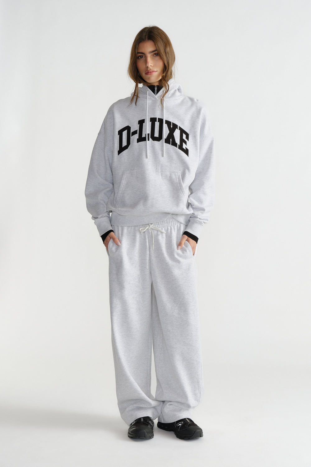 Woman wearing light grey hoodie with black lettering and matching wide-leg sweatpants with black sneakers