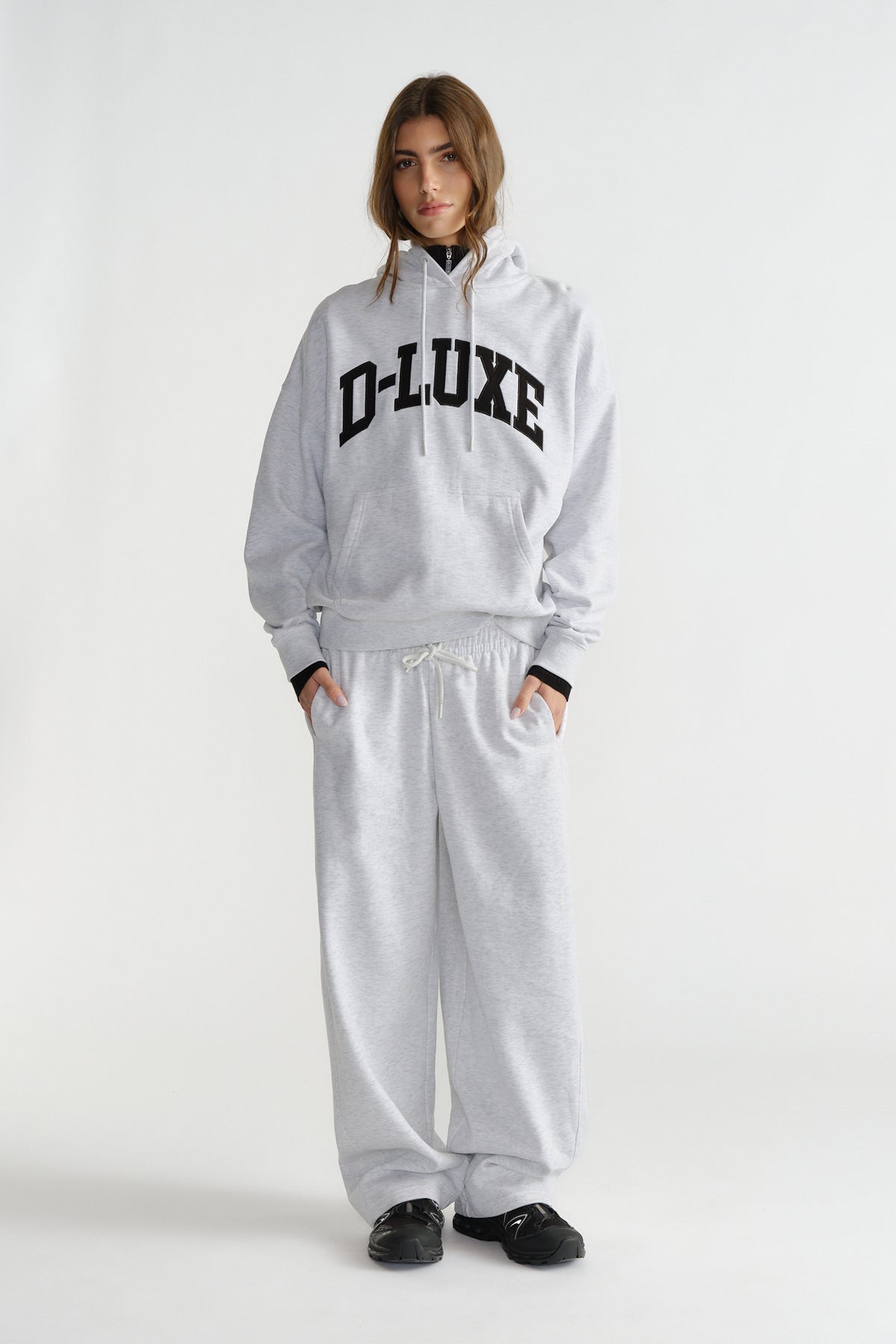 Woman wearing light grey hoodie with black lettering and matching wide-leg sweatpants with black sneakers