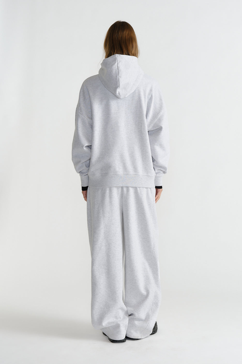Rear view of a model wearing a relaxed light grey hoodie and matching wide-leg pants in casual style
