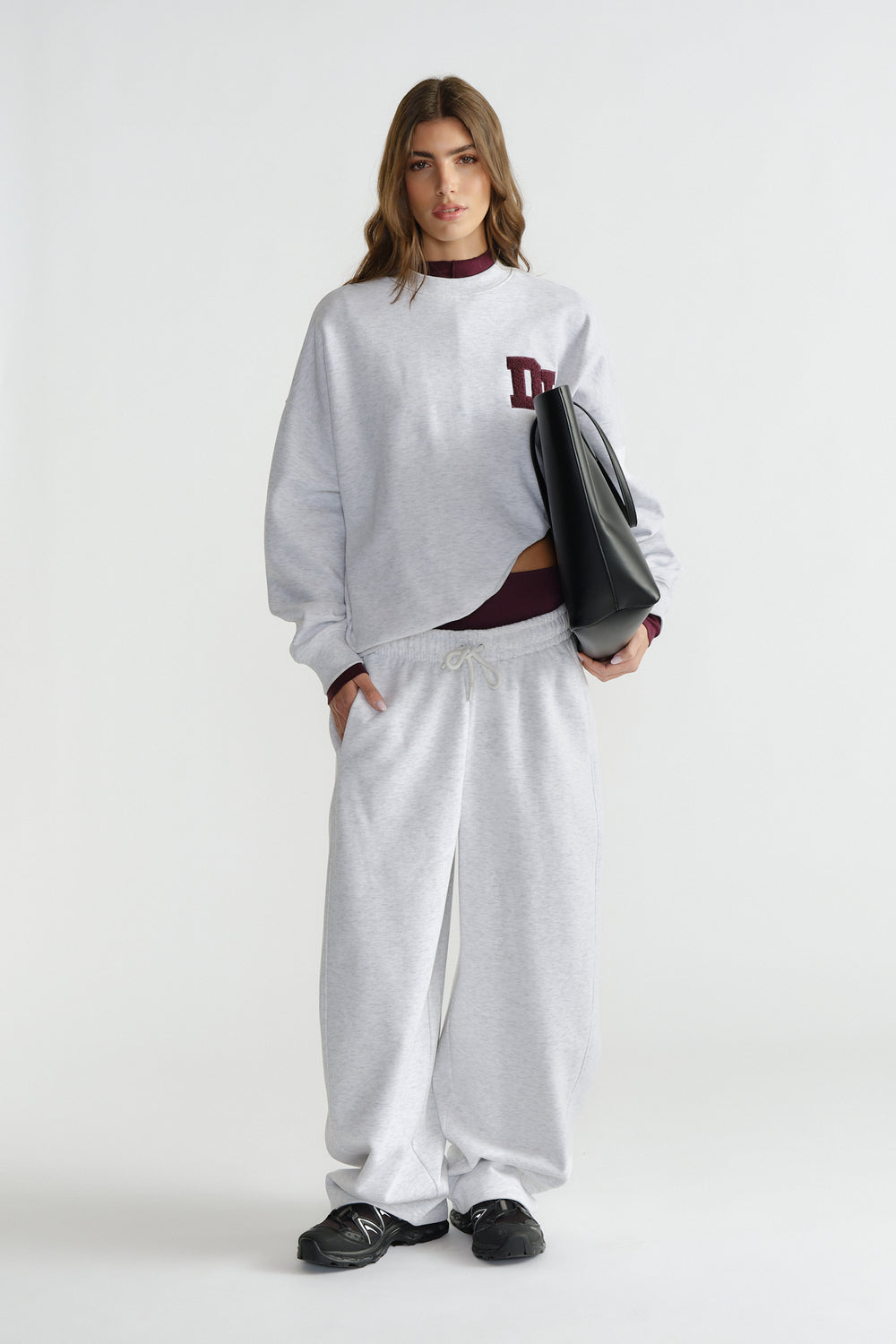 Woman in light grey sweat set with burgundy top details, holding a large black tote, styled with black sneakers