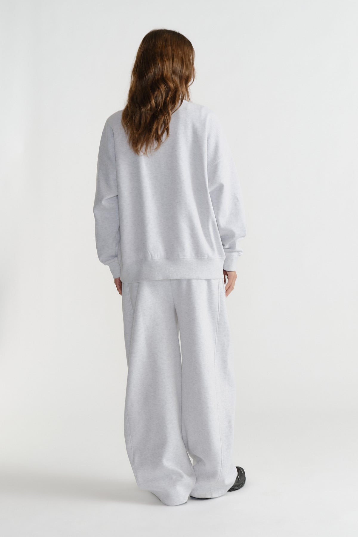Model seen from behind wearing a relaxed light grey crewneck sweatshirt and matching wide-leg sweatpants.