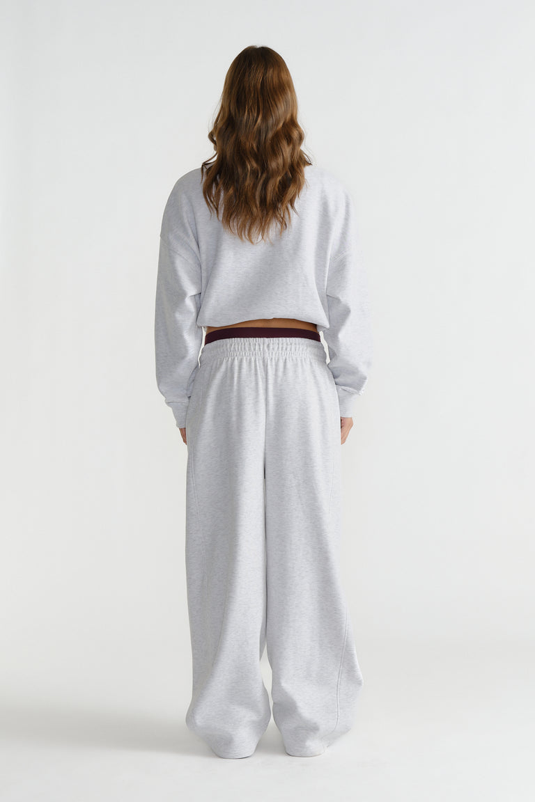 Back view of a woman wearing relaxed light grey track pants with an elastic waistband and a cropped sweatshirt