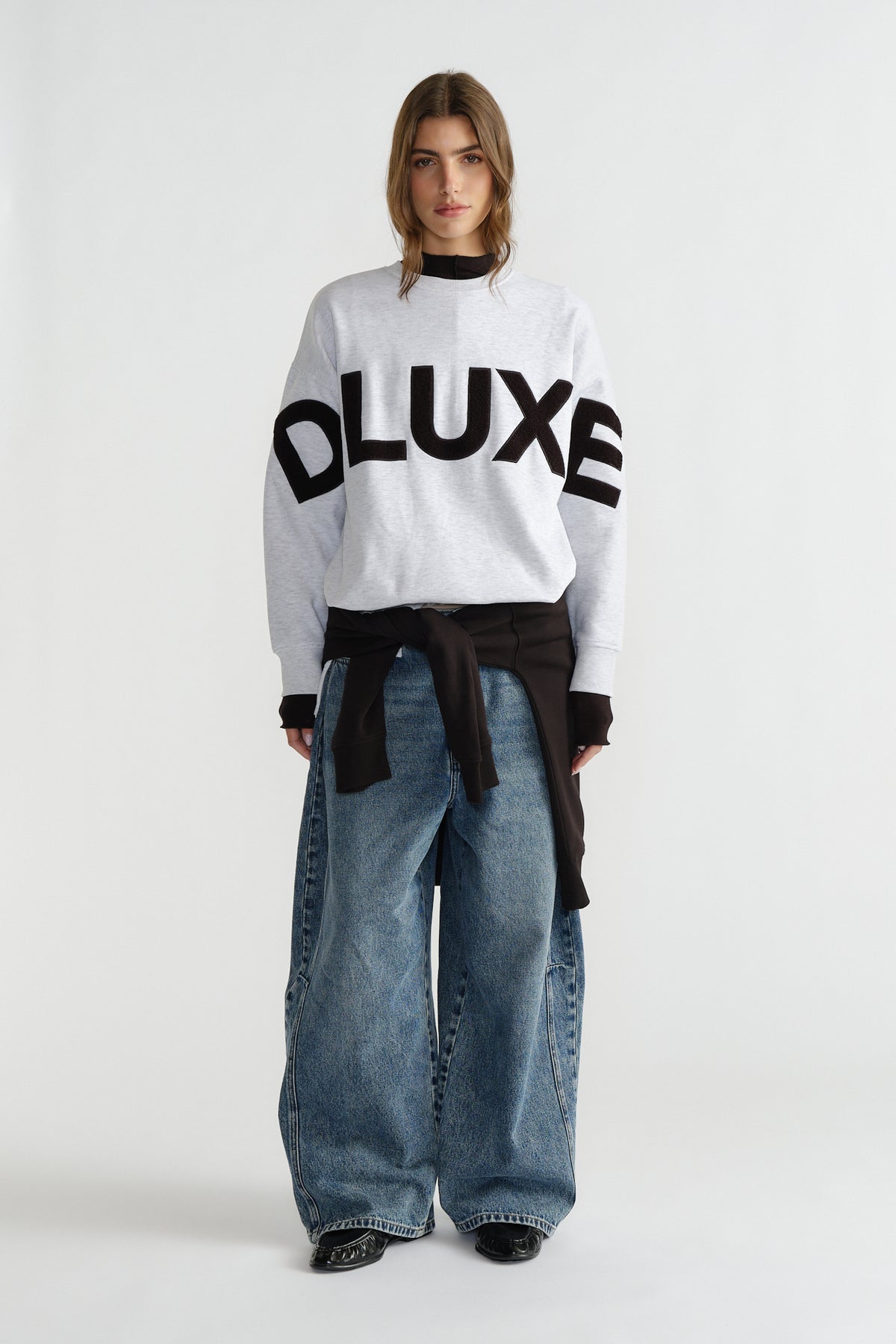 Woman wearing light grey sweatshirt with bold black lettering paired with wide-leg faded blue jeans and black layer underneath