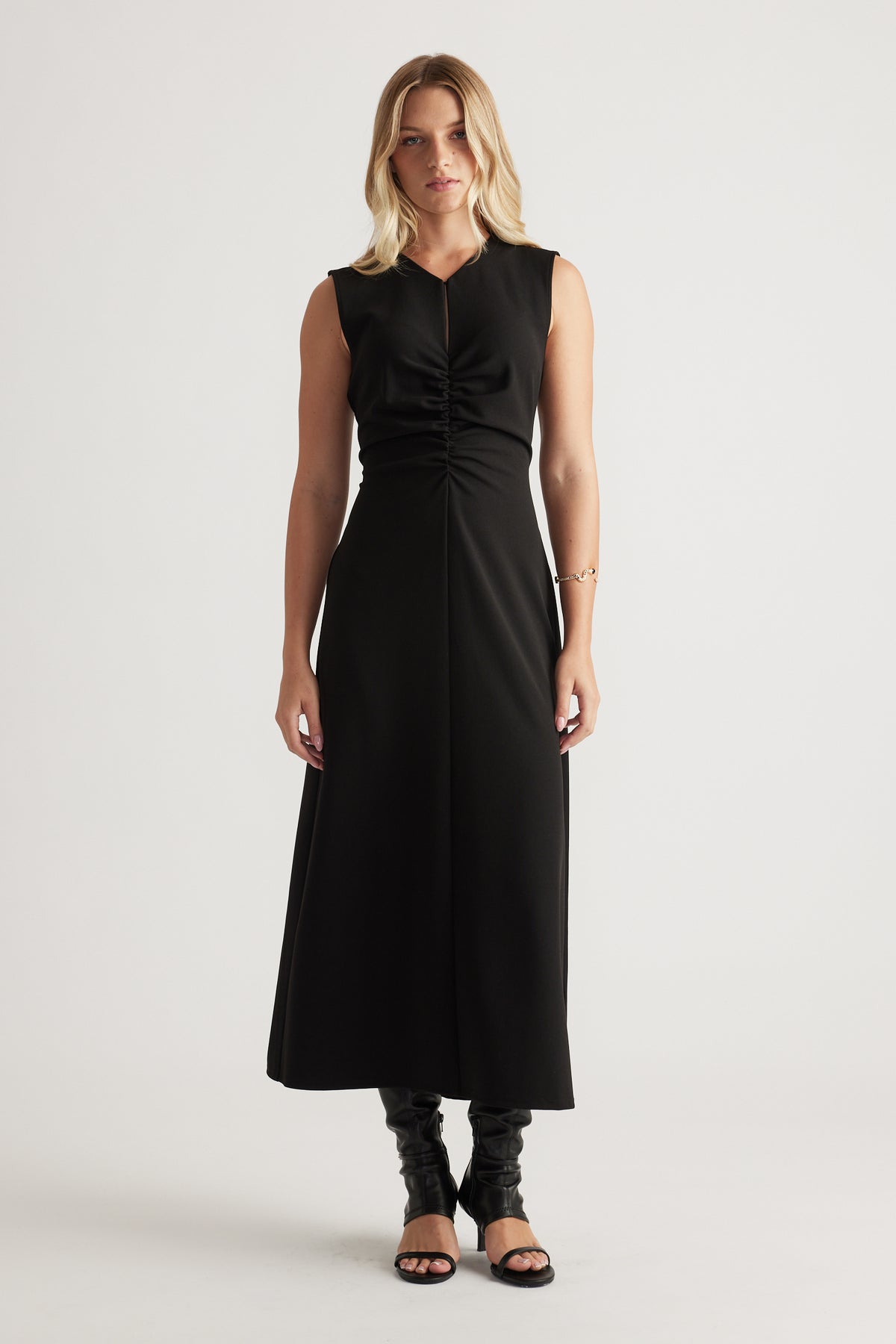 Sleeveless black midi dress with ruched front detail, flattering fitted waist and flowing skirt worn with heeled sandals.