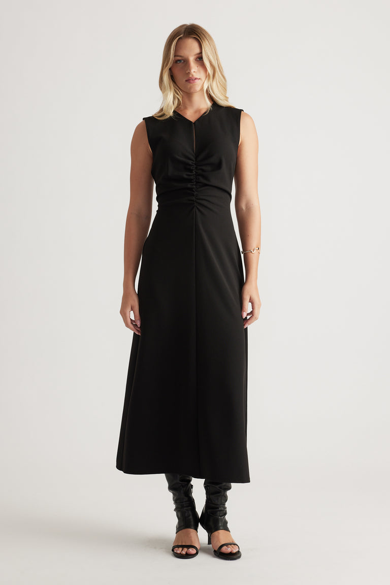 Sleeveless black midi dress with ruched front detail, flattering fitted waist and flowing skirt worn with heeled sandals.