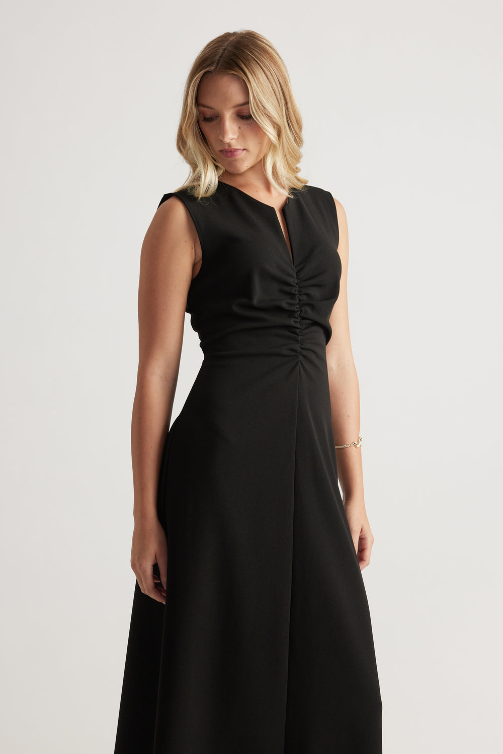 Sleeveless black midi dress with ruched front detail and subtle V-neck, styled for elegant everyday wear.