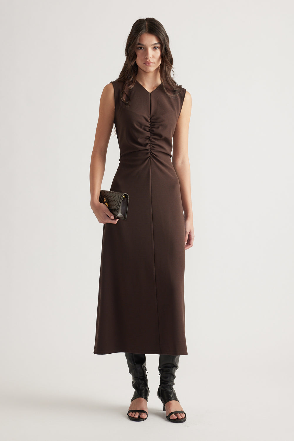 Woman wearing a sleeveless chocolate brown ruched midi dress styled with black heeled sandals and a quilted clutch bag
