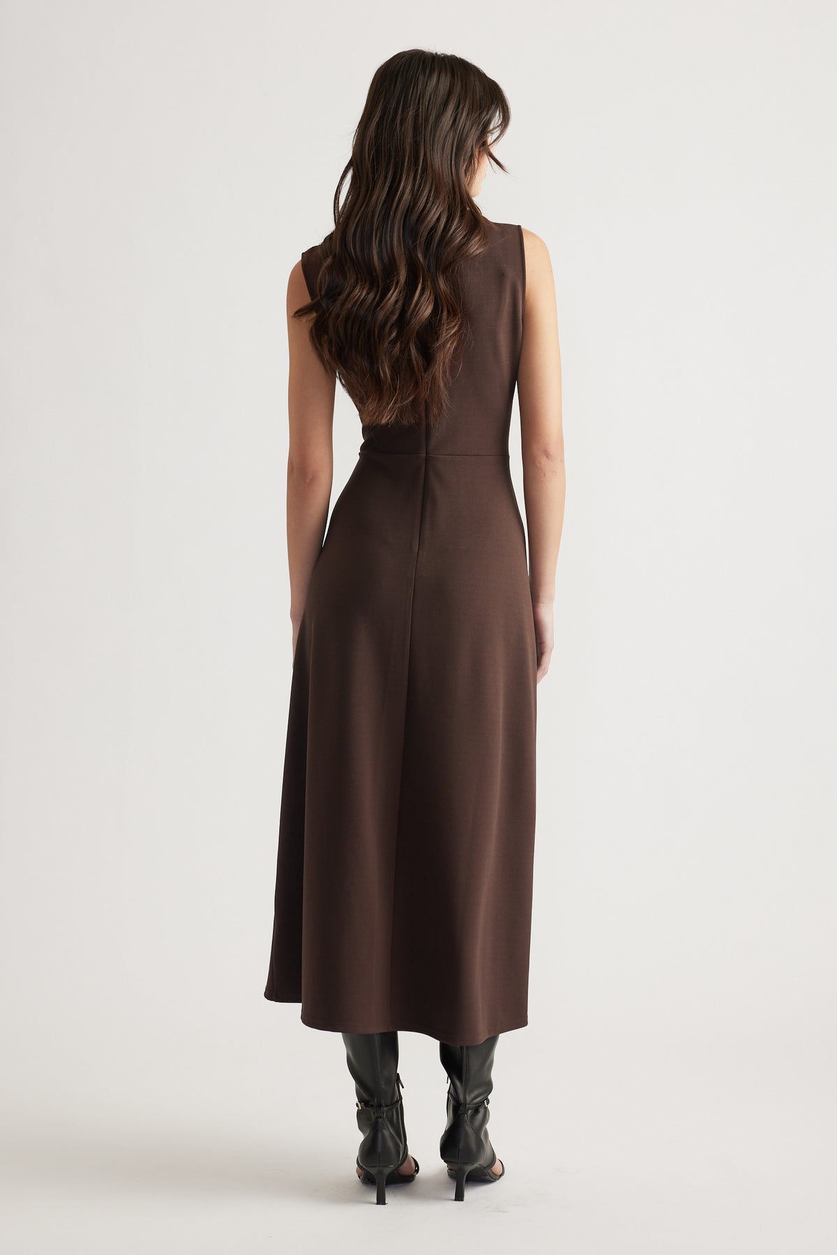 Back view of a woman wearing a sleeveless chocolate brown midi dress paired with black heeled boots