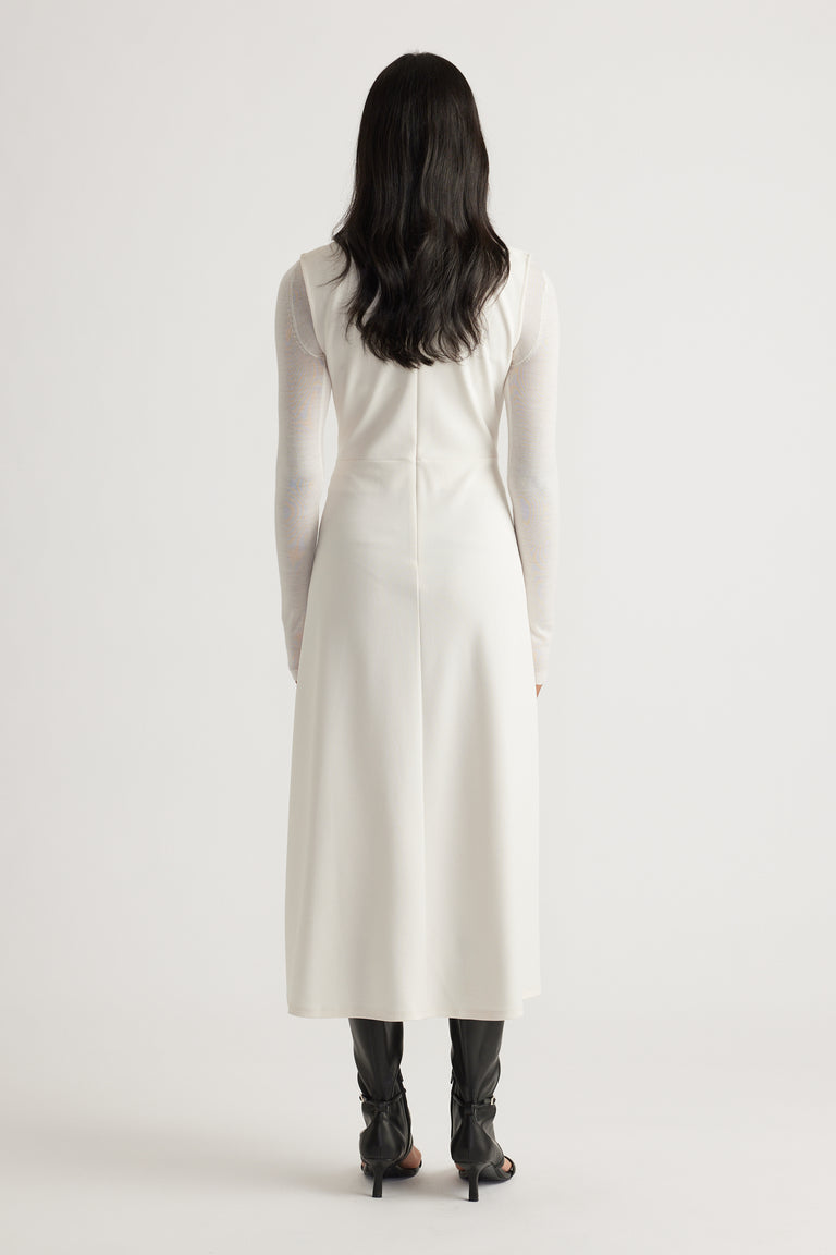 Back view of a sleeveless white midi dress worn over a sheer long-sleeve top paired with black heeled boots