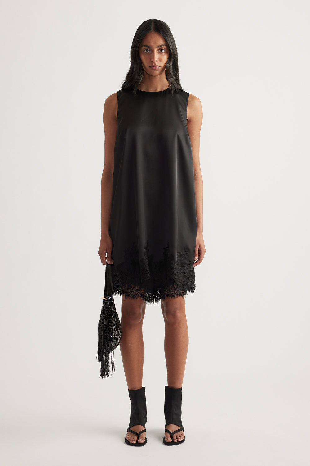 Woman wearing a black sleeveless shift mini dress with lace trim hem and round neckline