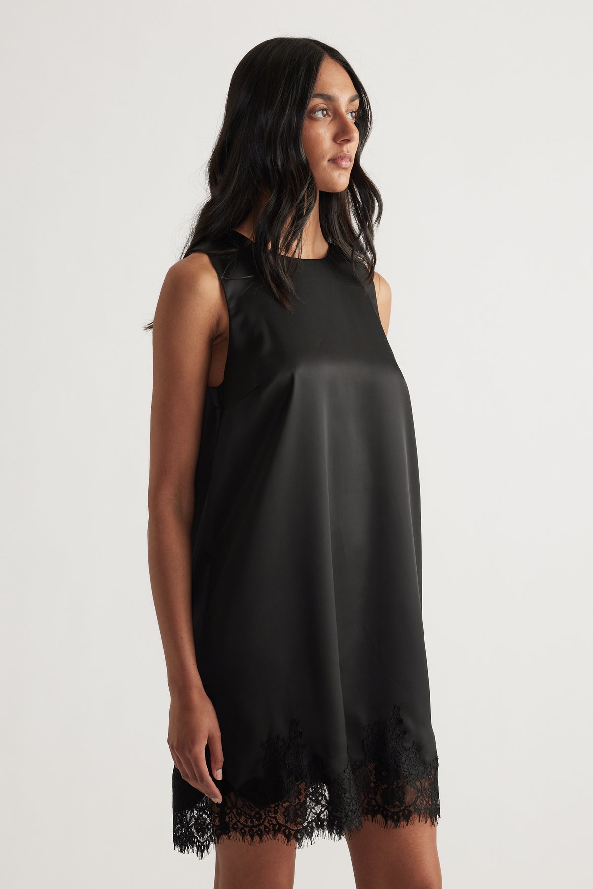 Woman wearing a black sleeveless shift mini dress with a round neckline and lace trim hem