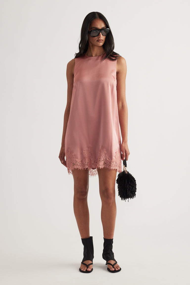 Woman wearing a pink sleeveless shift mini dress with a lace hem and black sandals