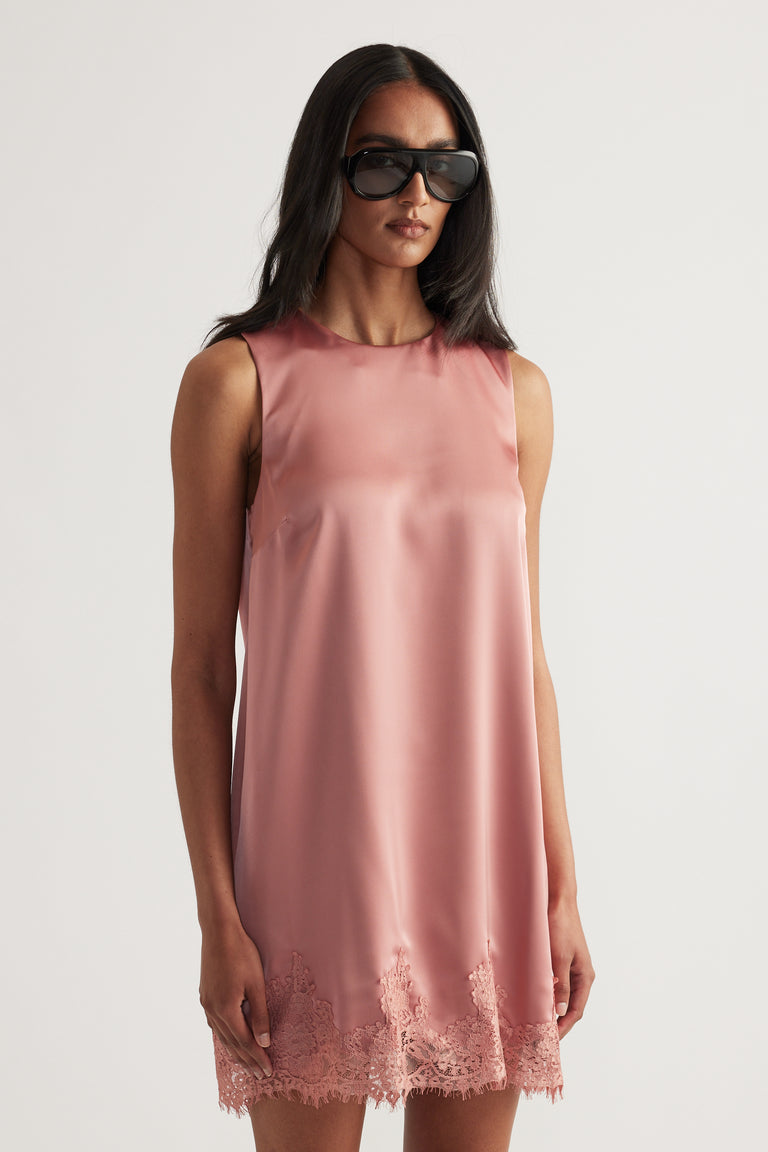 Woman wearing a pink sleeveless shift mini dress with a round neckline and lace trim hem