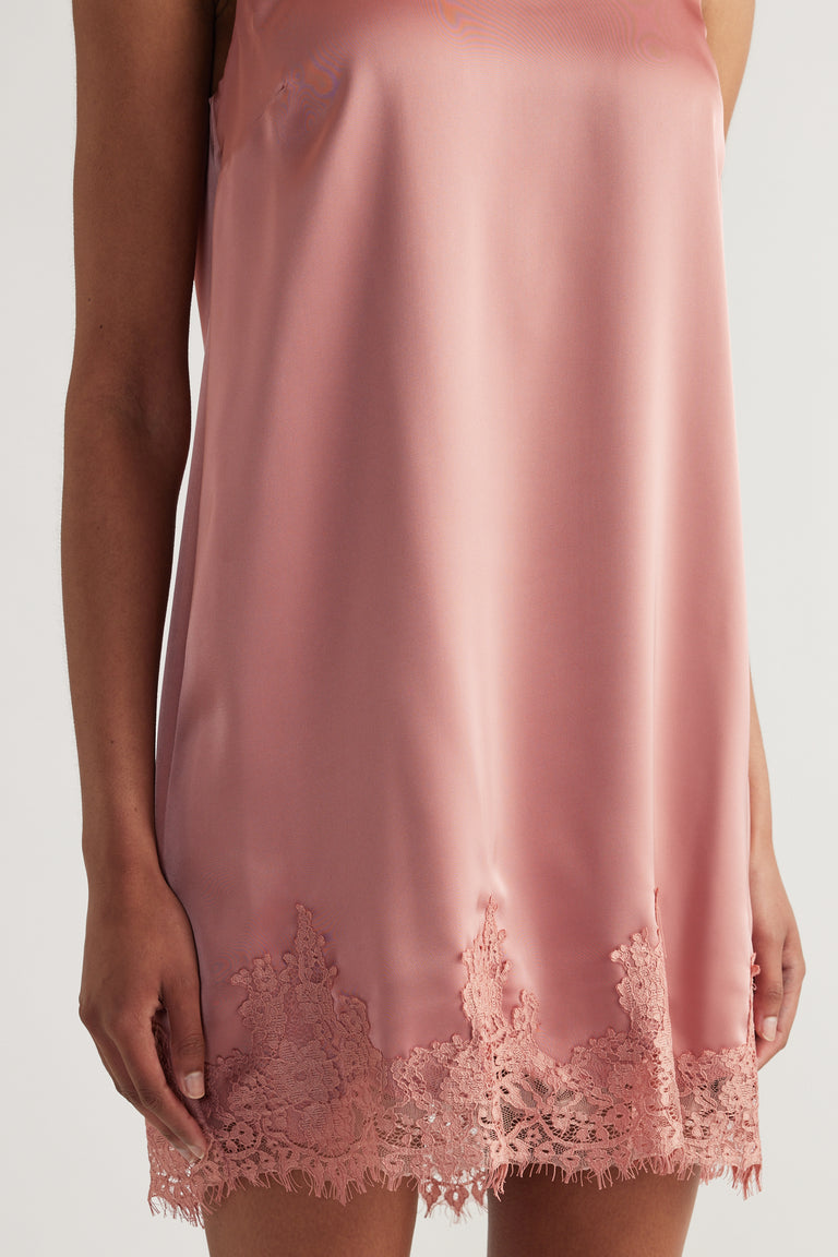 Model wearing a dusty pink sleeveless shift dress with delicate lace trim along the hem