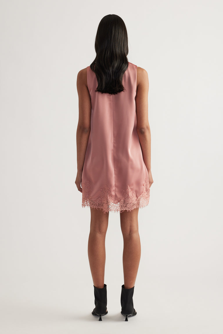 Model viewed from behind wearing a dusty rose sleeveless shift mini dress with a lace trimmed hem and black ankle boots
