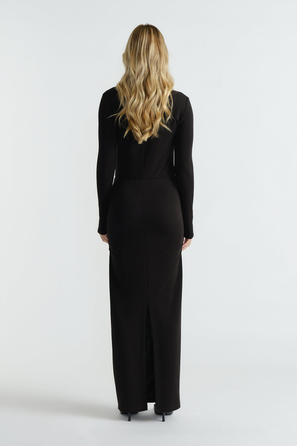Slim-fitting black long-sleeve midi dress with subtle back slit, styled for an elegant and timeless silhouette.