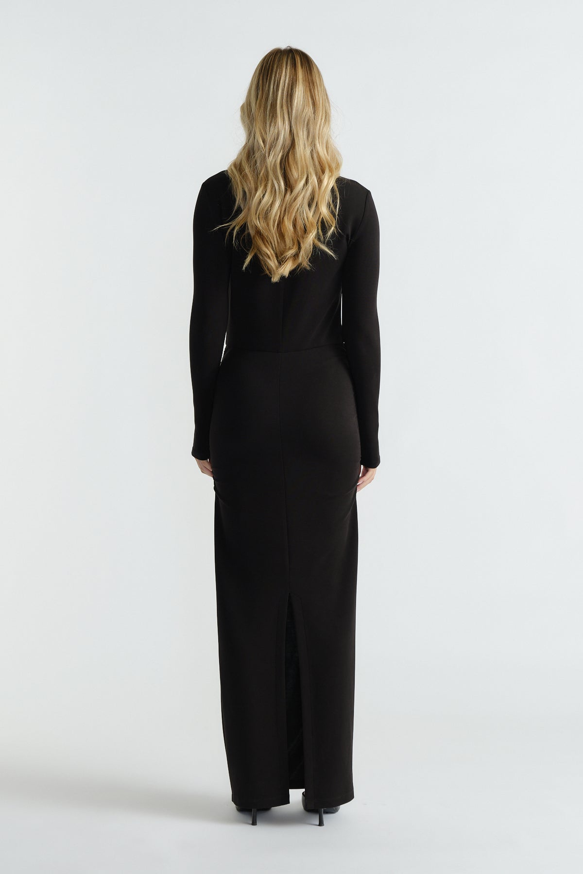 Slim-fitting black long-sleeve midi dress with subtle back slit, styled for an elegant and timeless silhouette.