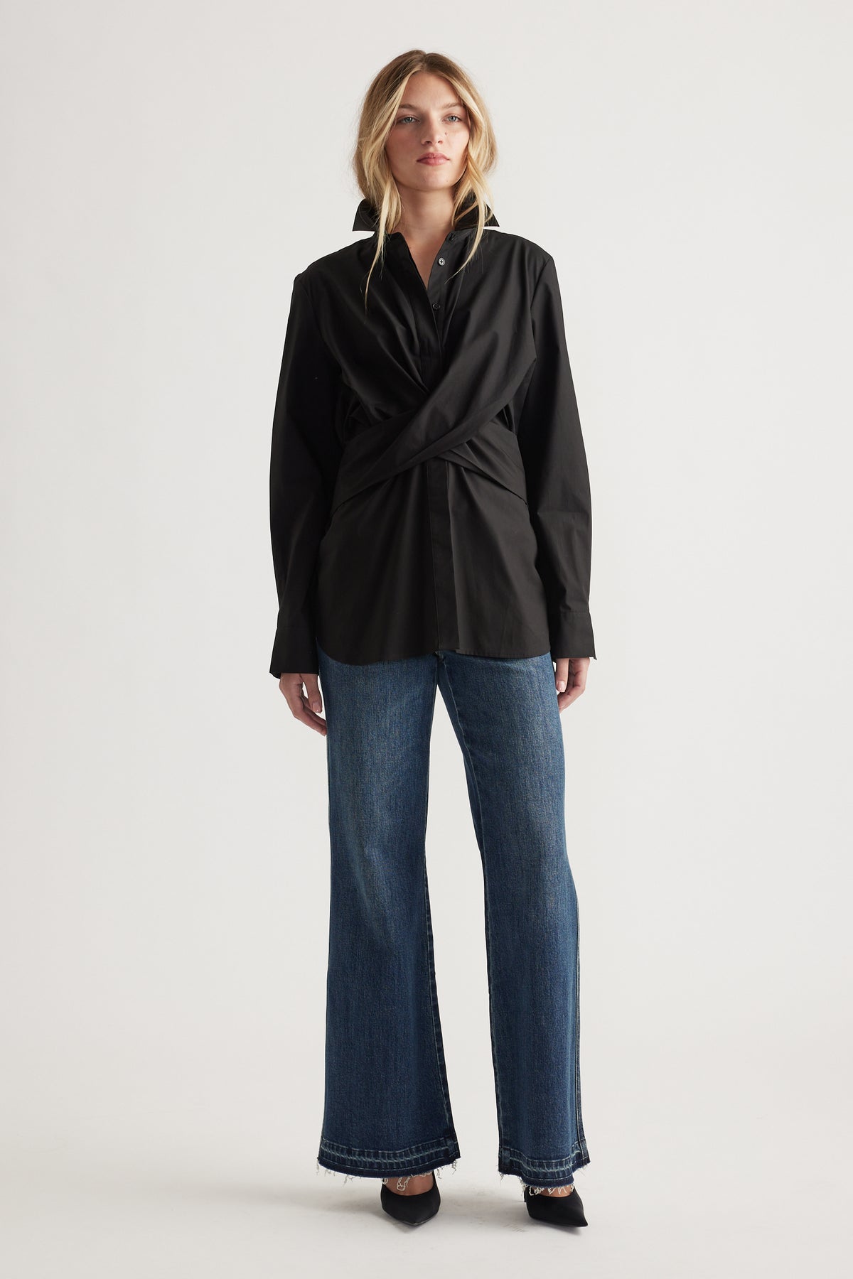 Woman wearing a black twist-front shirt paired with relaxed straight-leg denim jeans and pointed black heels