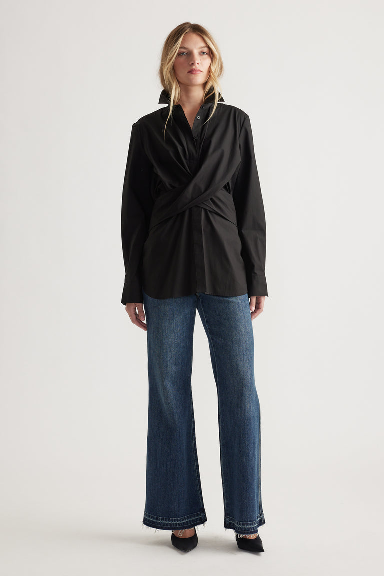 Woman wearing a black twist-front shirt paired with relaxed straight-leg denim jeans and pointed black heels