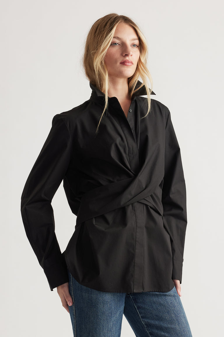 Woman wearing a black long-sleeve shirt with a twisted front detail paired with classic blue denim jeans