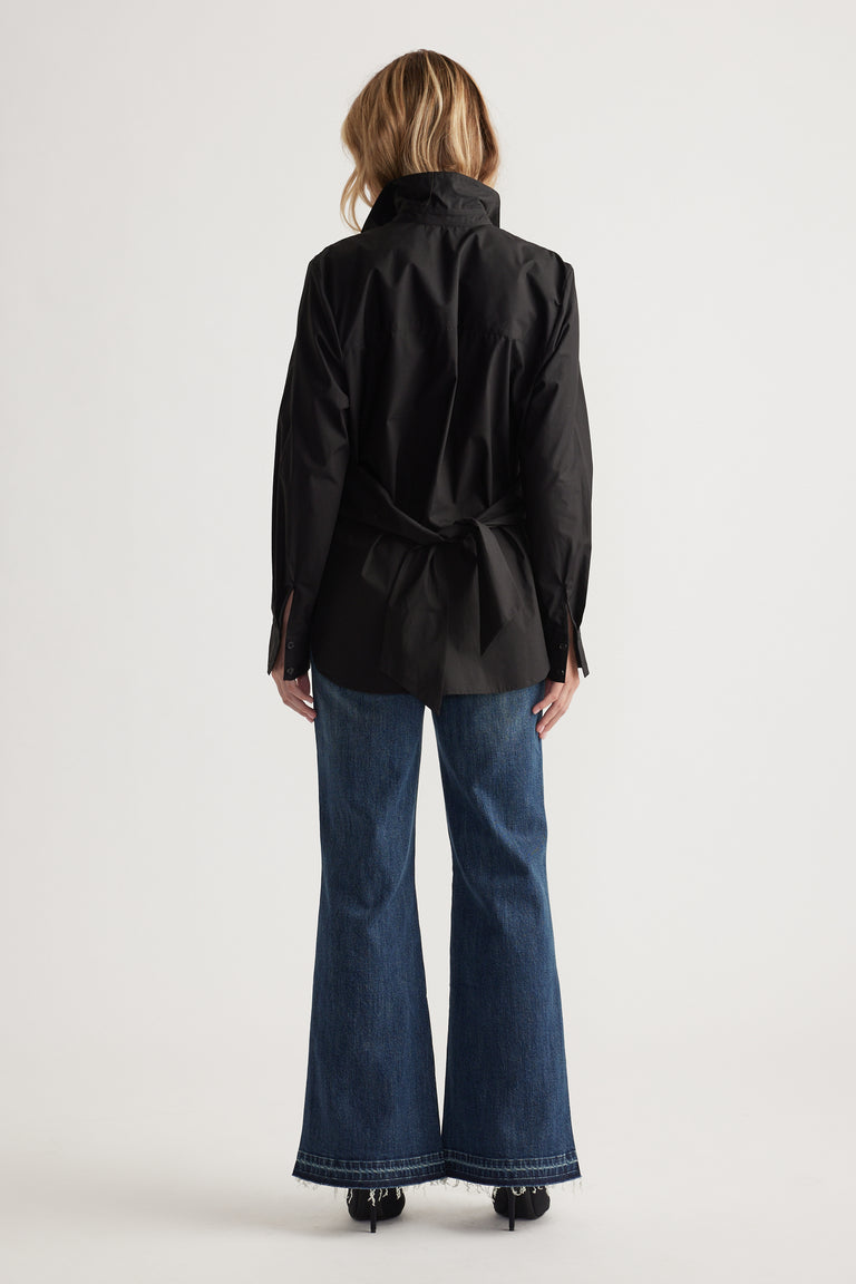 Woman wearing a black long-sleeve shirt with a tied back detail paired with high-waisted wide-leg blue jeans