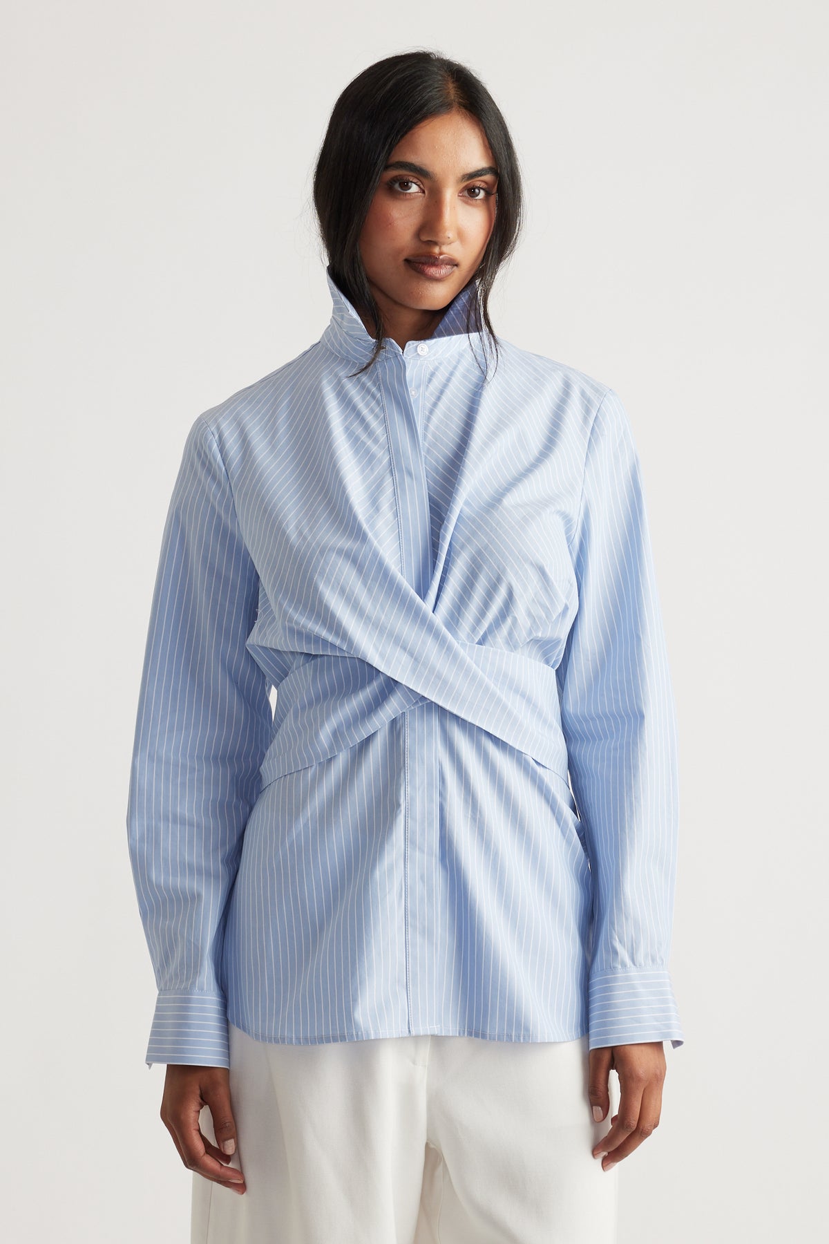 Light blue pinstripe shirt with wrap front detail and structured collar, styled for a modern everyday look