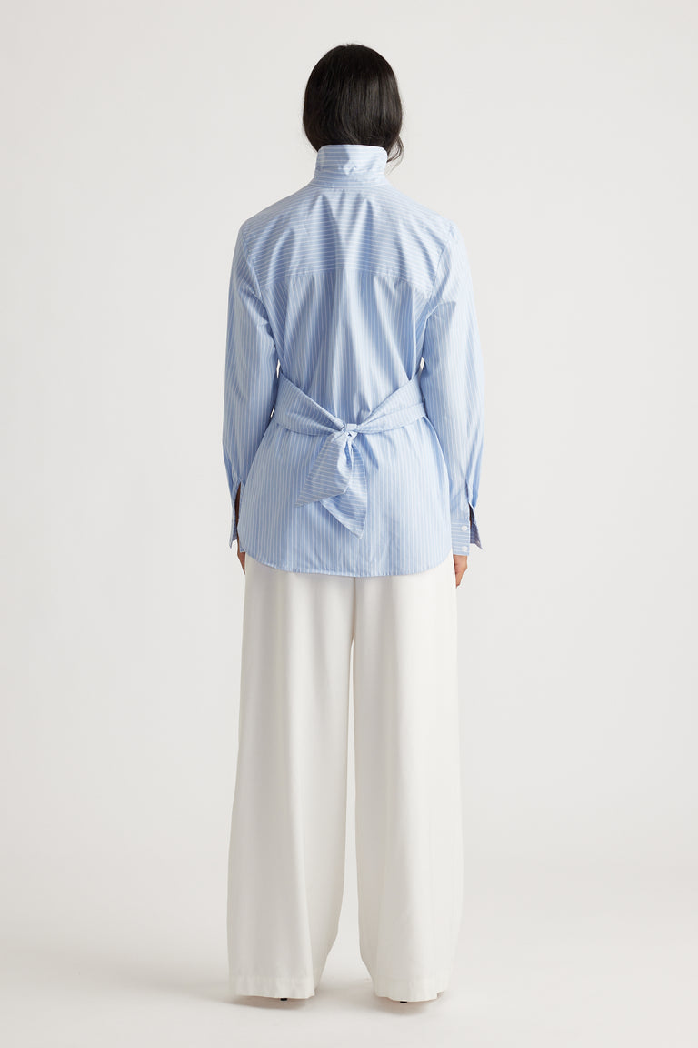 Woman wearing a light blue striped shirt with tie detail at the back paired with wide-leg white pants for an elegant look