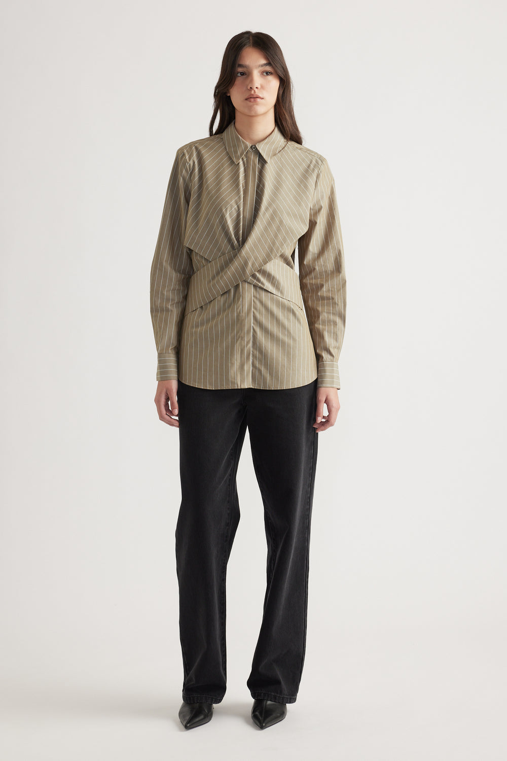 Woman wearing a striped beige button-up shirt with a unique wrap detail, paired with straight black pants and pointed shoes