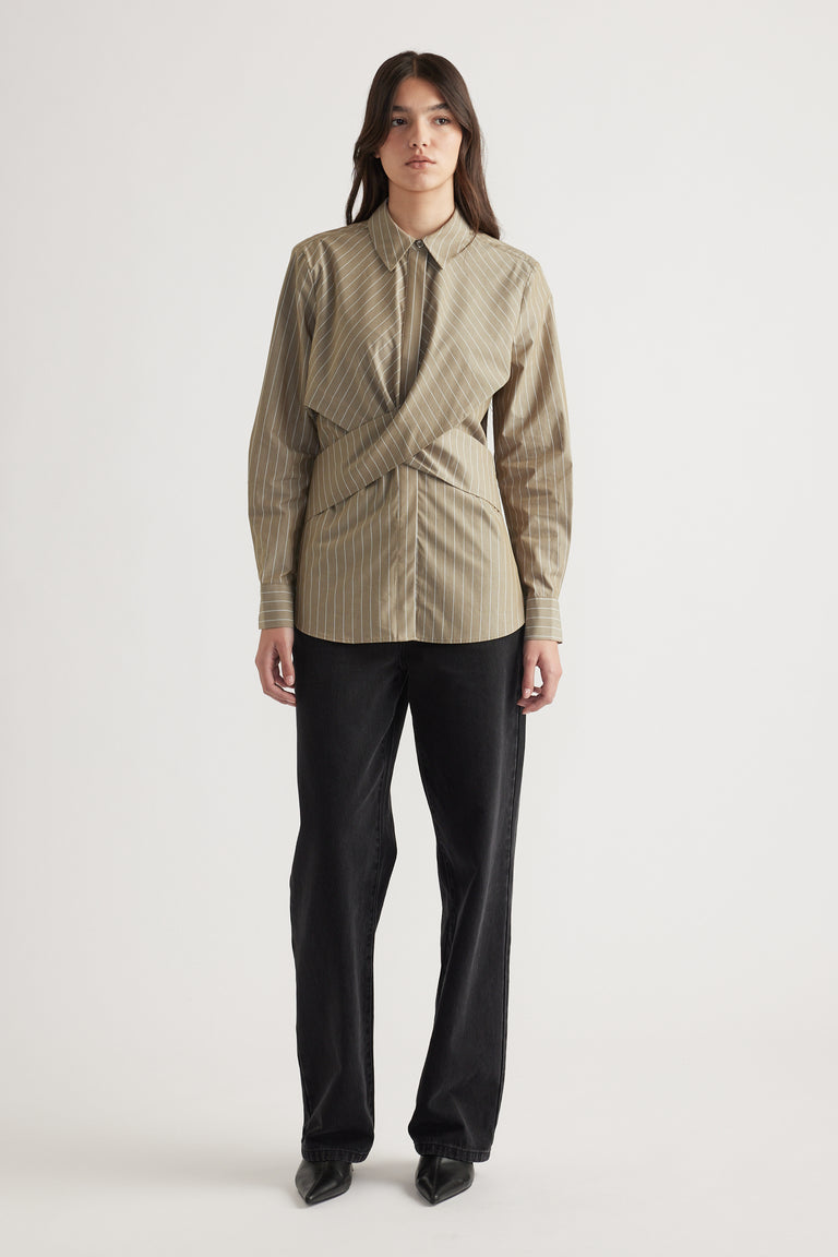 Woman wearing a striped beige button-up shirt with a unique wrap detail, paired with straight black pants and pointed shoes