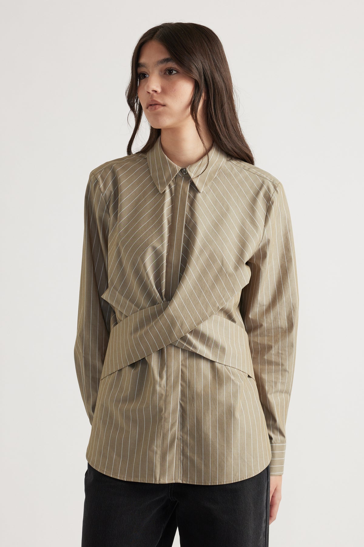 Woman wearing beige pinstripe shirt with unique twist front detail paired with black pants against plain background
