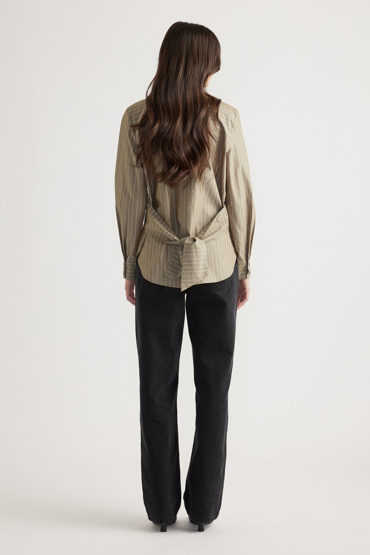 Woman wearing a neutral striped shirt with a tied detail at the back paired with relaxed black wide-leg jeans