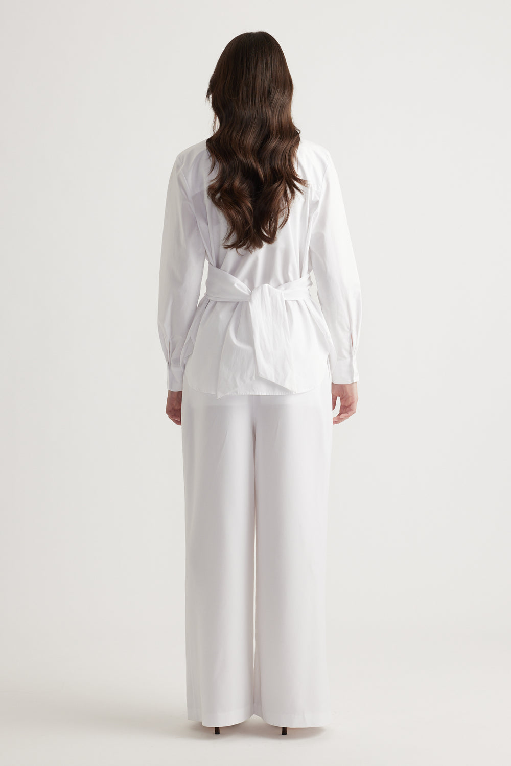 Back view of a woman wearing a white tie-back shirt paired with wide-leg white pants for a clean, elegant look.