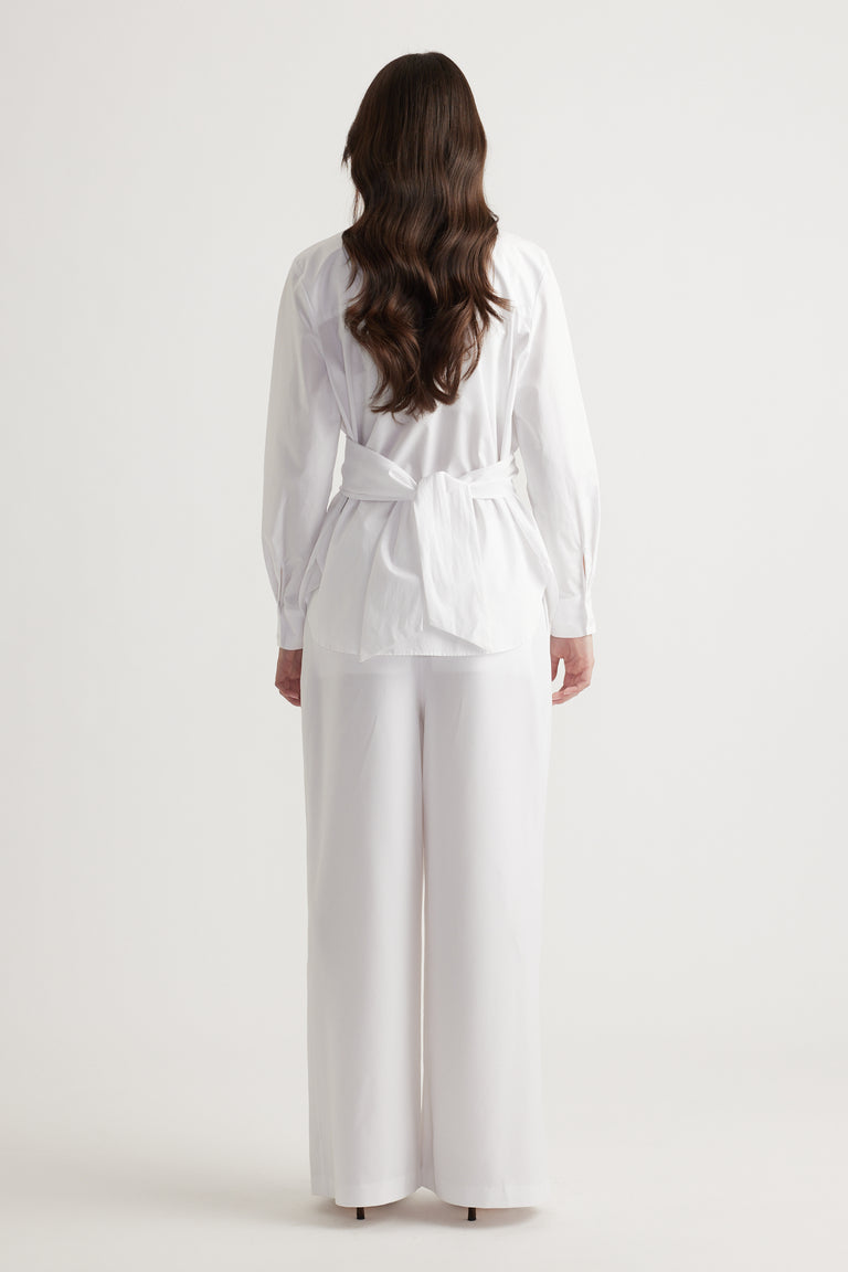 Back view of a woman wearing a white tie-back shirt paired with wide-leg white pants for a clean, elegant look.