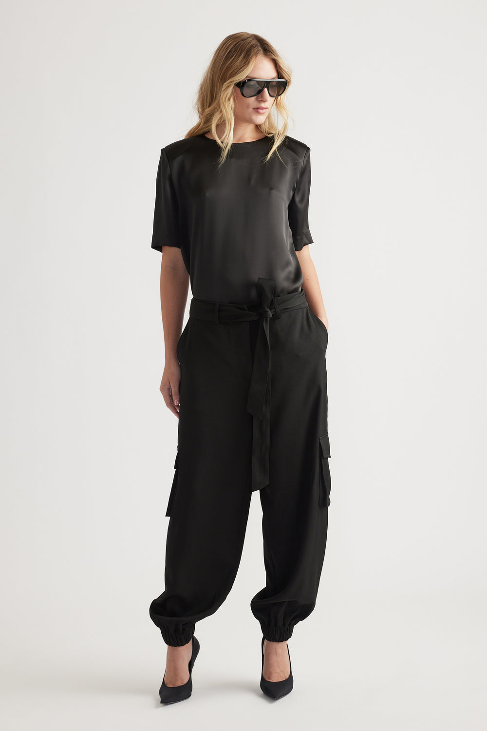 Woman wearing a black satin top with shoulder pads paired with relaxed cargo pants and black pointed heels
