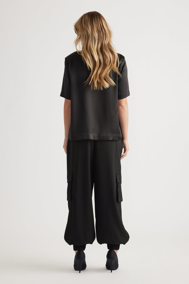 Woman seen from behind wearing a loose black satin top paired with wide-leg black cargo pants and black heels